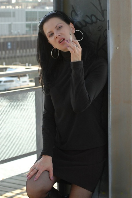 Fully clothed brunette lights up a cigarette with her sunglasses atop her head 80845498