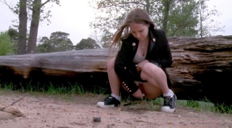 Caucasian girl Nastya squats for a pee by a rotting log on a patch of sand 98348234